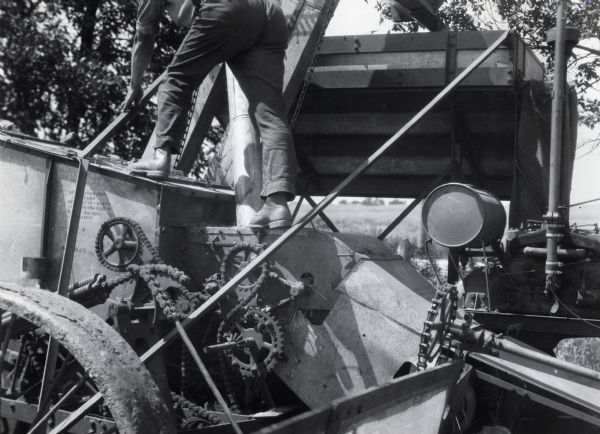 A man is climbing on a moving harvester-thresher (combine), illustrating an agricultural hazard for International Harvester's Agricultural Extension Department.