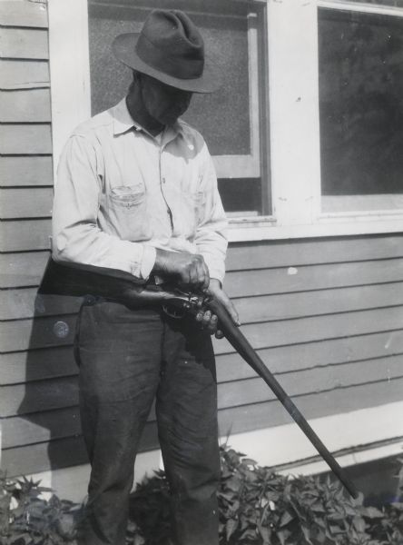 A man removing shotgun shells from a firearm before placing it in storage at International Harvester's Hinsdale experimental farm.