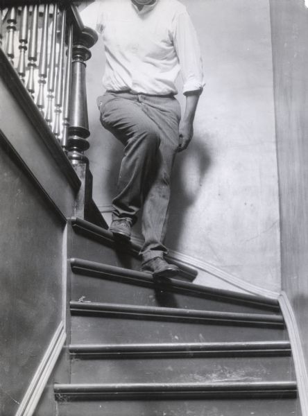 A man descending a curved staircase inside a building. The photograph was taken for International Harvester's Agricultural Extension Department to illustrate the hazards of unmaintained stairs.