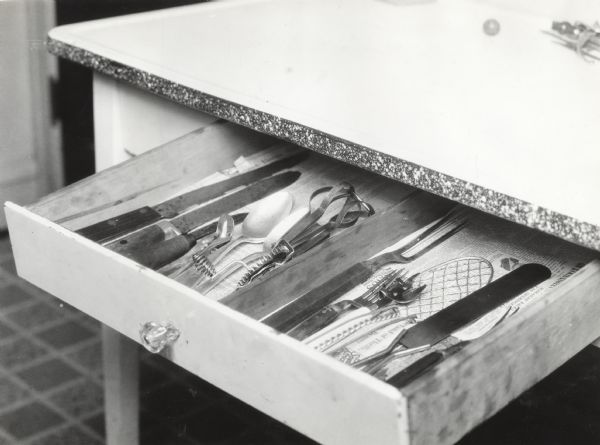 View from above of an open drawer revealing sharp knives mixed in with other kitchen utensils.