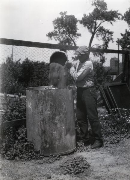 A man pouring ashes from a bucket into a larger metal container.