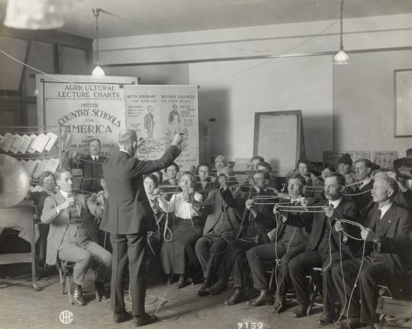 Rope tying demonstration for a group of rural school teachers. Original caption reads: "County Supt. Tobin, Country Life Director, and rural school teachers of Cook county, perfect their knowledge of the Vitalized work in the office of the Agricultural Extension Department, Harvester Building."