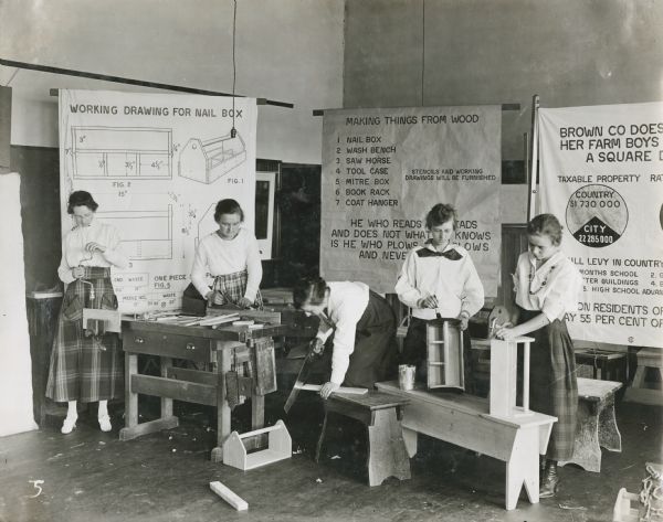 Group of young women, probably students, assembling wooden nail boxes and benches in a classroom.