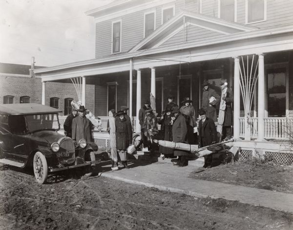 "Crew No. 2" of the Agricultural Extension's "Alfalfa Campaign" standing out in front of residential home with equipment, including rolled up lecture charts.