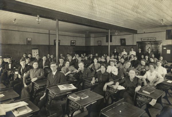 Group of male and female students seated at desks in the assembly room of the School of Agriculture.