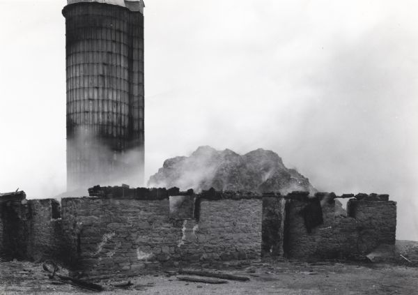 Smoke rises from the remnants of a barn and silo ruined by fire.