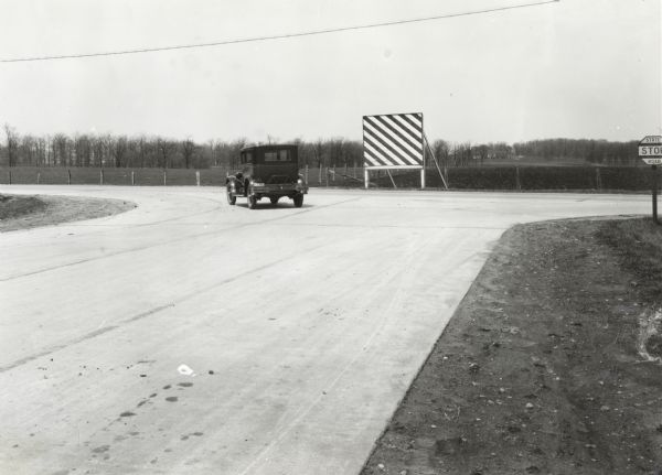 An automobile rounds a turn near several traffic signs placed along the edge of a paved state road.