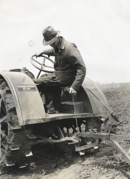 A man is adjusting the hitch of a McCormick-Deering 10-20 tractor with a hook while working in a field at International Harvester's experimental farm.