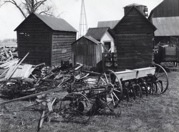 Exterior view of a barnyard littered with old farm machinery and piled wood.
