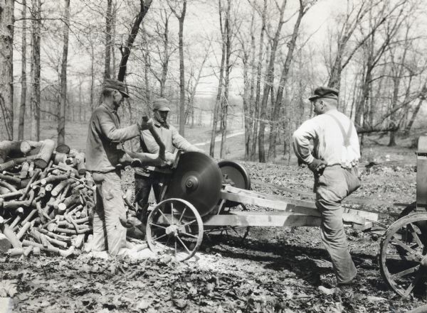 Three men use circular saws to cut wood in a forest. The tractor on the right appears to be providing belt-driven power to the saws.