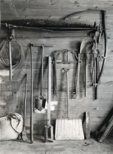 View of multiple farm implements organized against a wall inside a barn or shed at Cutten Farms.