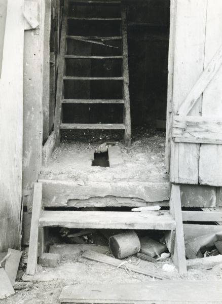View of the door leading into a grainery, with broken floorboards and wooden steps.