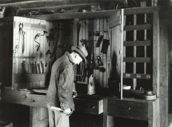 A man wearing a hat and denim jacket stands near a tool cabinet in a barn or workshop while looking through a drawer at Cutten Farms.