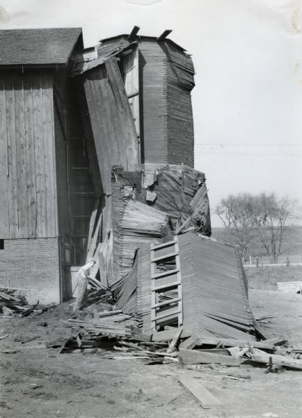 A man examines the base of a fallen wood silo.