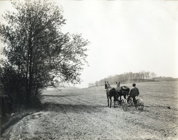 A farmer is using a planter drawn by a team of two horses to work in a farm field.