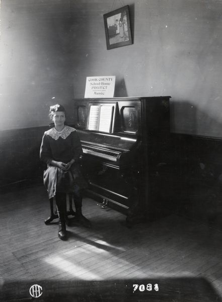 Portrait of a young woman, the prize winner of the Cook County school-home project in music, sitting at a piano.