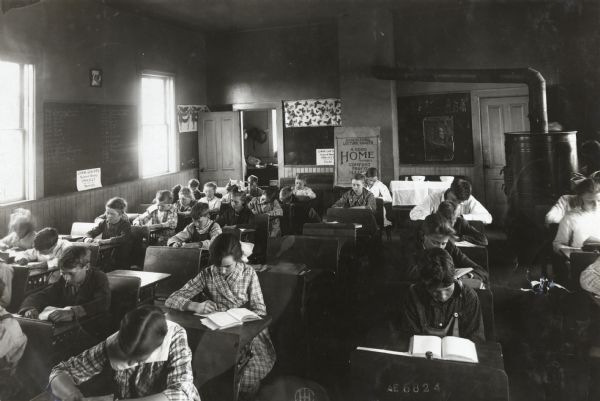 View from front of a classroom of students sitting at their desks in the Sedan Prairie School. A large round woodstove is in the back right corner of the room.