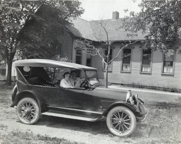 Two rural school teachers, identified as "Miss Sullivan" and her assistant "Miss Brady," seated in a parked automobile outside a building.