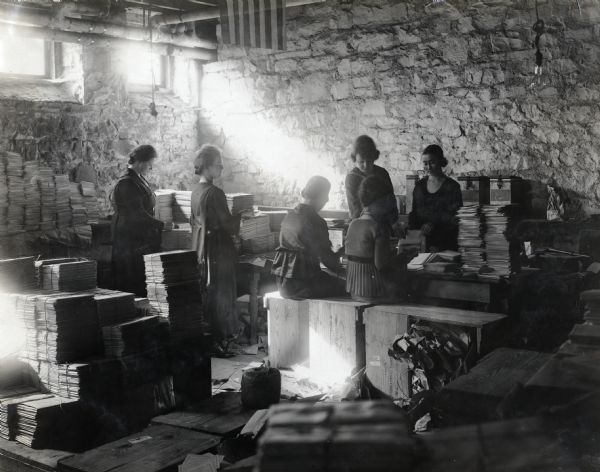 A group of women are preparing stacks of literature on the "Vitalized Agriculture Program" in the basement of a building. The program was administered by International Harvester's Agricultural Extension Department.