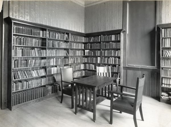 District school library with bookshelves along the walls near a window, and a table and chairs arranged in front of them.