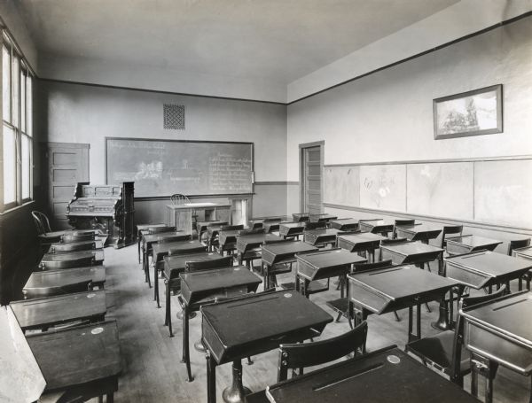 Interior view of a school room at Mohegan Lake Public School, filled with rows of desks, an organ, and several chalkboards. The text on the chalkboard reads: "Mohegan Lake Public School. June 2, 1912."