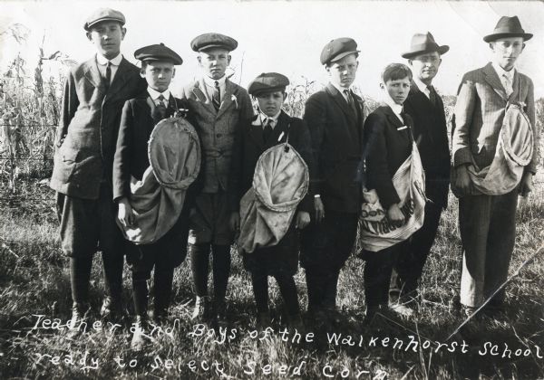 A group of boys from the Walkenhorst School holding fabric bags while posing in a field with their instructor on their way to select seed corn.