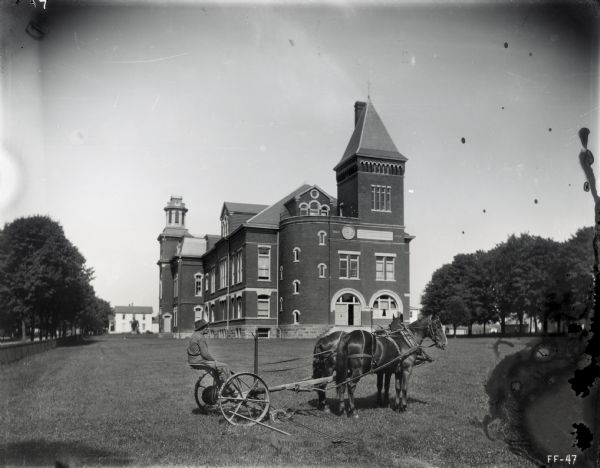 A man and a McCormick mower pulled by two horses are posing on the lawn of a building marked "State Normal School." The inscriptions on either side of the building's clock and sign reads: "1860" and "1890."