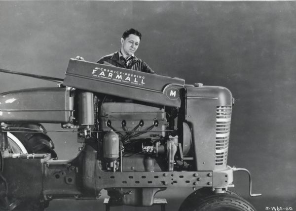 Man inspecting a Farmall M tractor in a studio. Decals are on the right side of the front of the tractor.