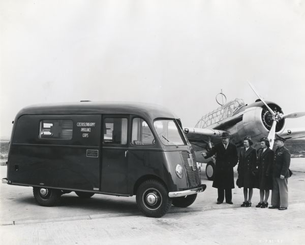 A group of two men and two women stand near an International D-15-M (Metro) truck sold to Czechoslovakian Relief for service with the Czechoslovakian Army in England. It is parked on an airstrip in front of an airplane.