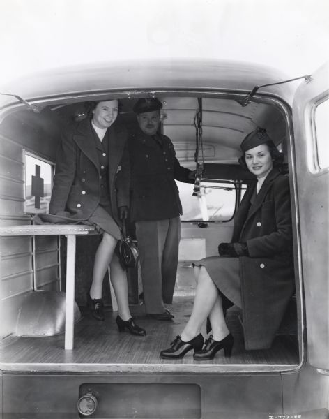 Two TWA hostesses, Ruth Ellison and Eula Walker, are sitting inside an International D-15-M (Metro) truck sold to Czechoslovakian Relief for service with the Czechoslovakian Army in England while First Lieutenant K.J. Fogle is standing behind them.