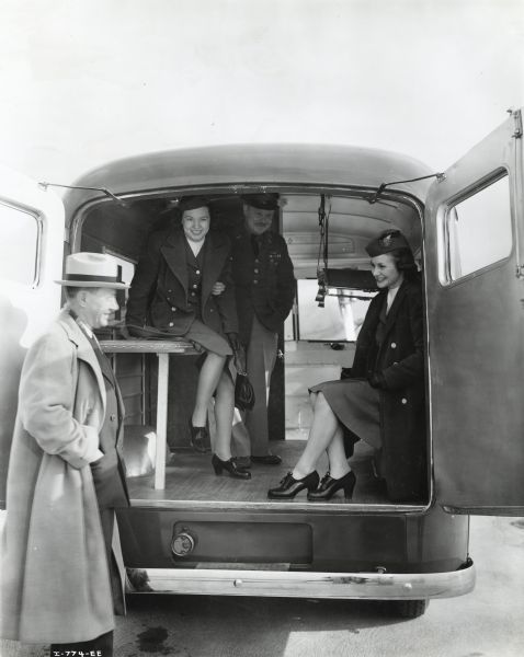 A uniformed First Lieutenant and two TWA air hostesses are sitting inside an International D-15-M (Metro) truck sold to Czechoslovakian Relief for service with the Czechoslovakian Army in England, while Frank Svoboda, manager of the Western Avenue International subbranch in Chicago, is standing near the ambulance's opened rear doors.