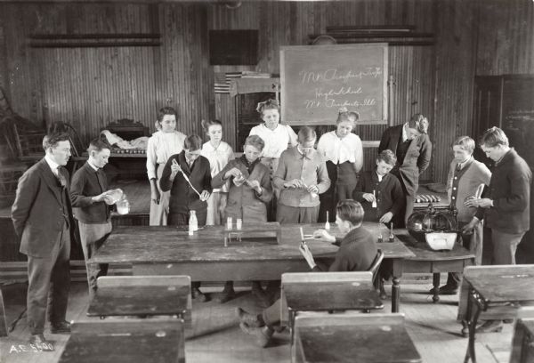 A group of children from Mount Prospect High School standing around a table in a classroom to conduct corn testing while their instructor is looking on from the left.