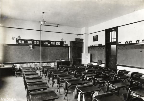 Interior view from back of room of a kindergarten classroom at Orange Township Consolidated School. Desks stand in rows, and chairs are lined at the front of the classroom beneath a chalkboard.