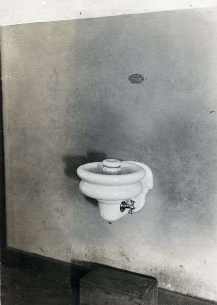 View of a drinking fountain inside Orange Township Consolidated School. There is a small plaque on the wall above the fountain.