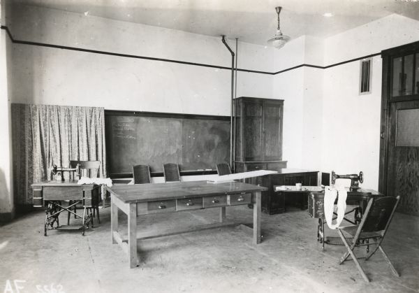 Interior view of tables, a chalkboard, and sewing machines inside the sewing room at Orange Township Consolidated School.
