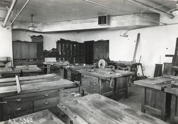 Interior view of the manual training room at Orange Township Consolidated School. Work tables stand throughout the room and the walls are lined with cabinets and a chalkboard.