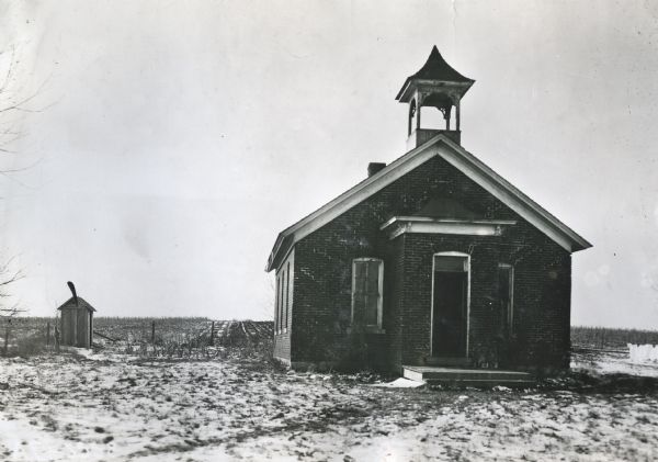 Exterior view of an abandoned district school building with a small shed or outhouse standing nearby.