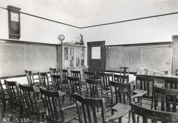 Interior view of chairs set up inside a classroom at the Orange Township Consolidated School. A clock and a chalkboard hang on the walls, and a globe and other school supplies stand on a cabinet near a door.