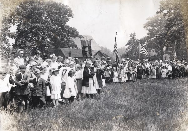 A group of children and adults, some holding American flags and Cook County banners, standing in a field to watch events at the Cook County School Festival.