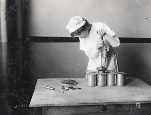 Mae Gribbon uses a soldering tool to seal tin cans in a home canning operation.