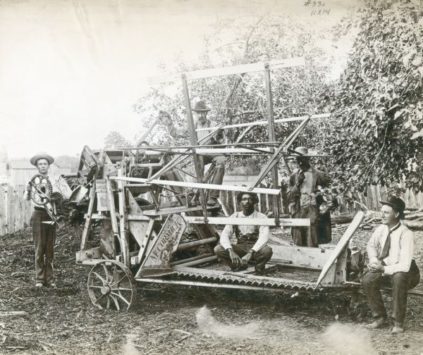 A group of five men are standing and sitting around a McCormick grain binder.