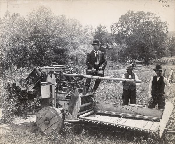 Three men posing with a piece of McCormick agricultural machinery, possibly a sickle bar mower (?). The writing on the machine reads, "McCormick H.M. Co. Harvester. Patented Mar 14 1876, Nov 26 1878, Jan 23 1883."