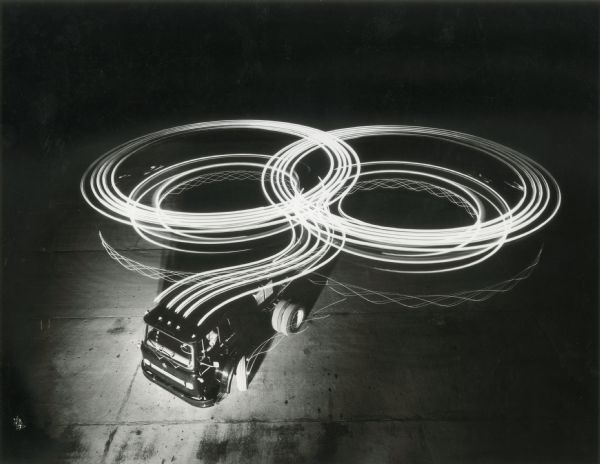 A man driving an International truck leaves circles of light from its head and tail lights in a parking lot during a long-exposure nighttime photograph.