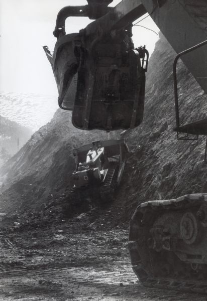 A man driving an International TD-30 crawler ascends a steep pile of dirt on a construction site. There is a front loader in the foreground.