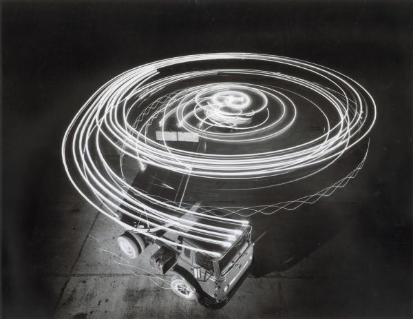 An International truck circles in what appears to be a parking lot at night, leaving behind a spiral of light from its head and tail lights during a long-exposure photograph.