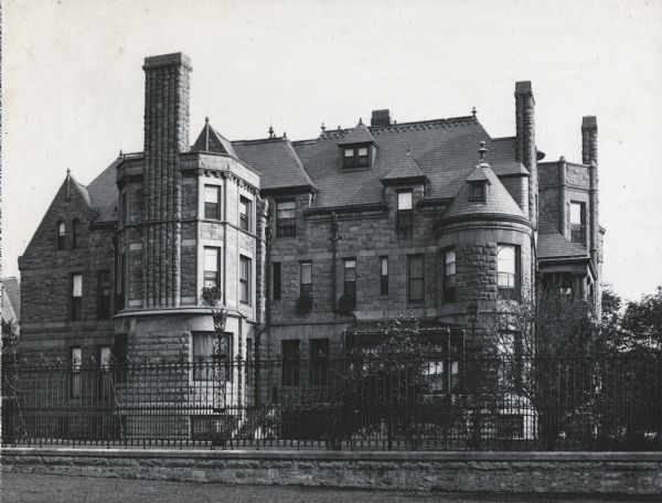 Exterior view of the residence of Harold McCormick and Edith Rockefeller McCormick surrounded by a fence made of stone and wrought iron. The home was built by Solon Spencer Beman and was located at 1000 Lake Shore Drive.
