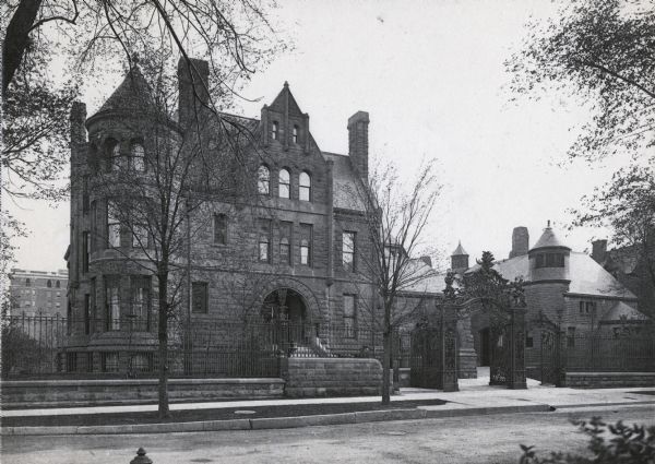 Exterior view of the residence of Harold McCormick and Edith Rockefeller McCormick. The home and yard are surrounded by stone and wrought-iron fencing with an elaborate gate opening to the walkway. The residence was built by Solon Spencer Beman and was located at 1000 Lake Shore Drive.
