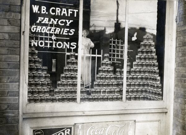 Canned goods labeled "Grown in Mississippi" are stacked in pyramids in the window of W.B. Craft grocery and notion store.