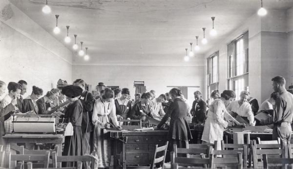 A group of men and women are gathered around tables in a classroom during a teachers short course. Some of the teachers are working with various tools, including saws and planes.