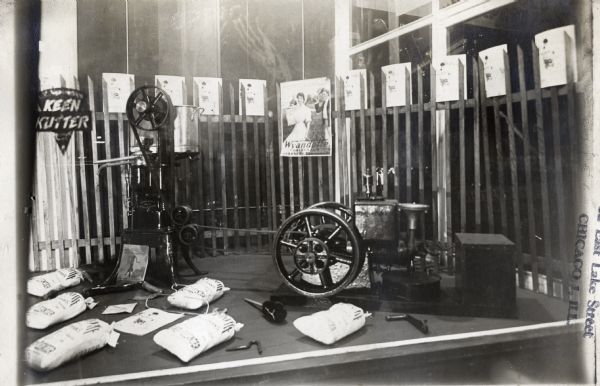 Burlap bags, a cream separator, a stationary engine and posters are used in a window display at a store.